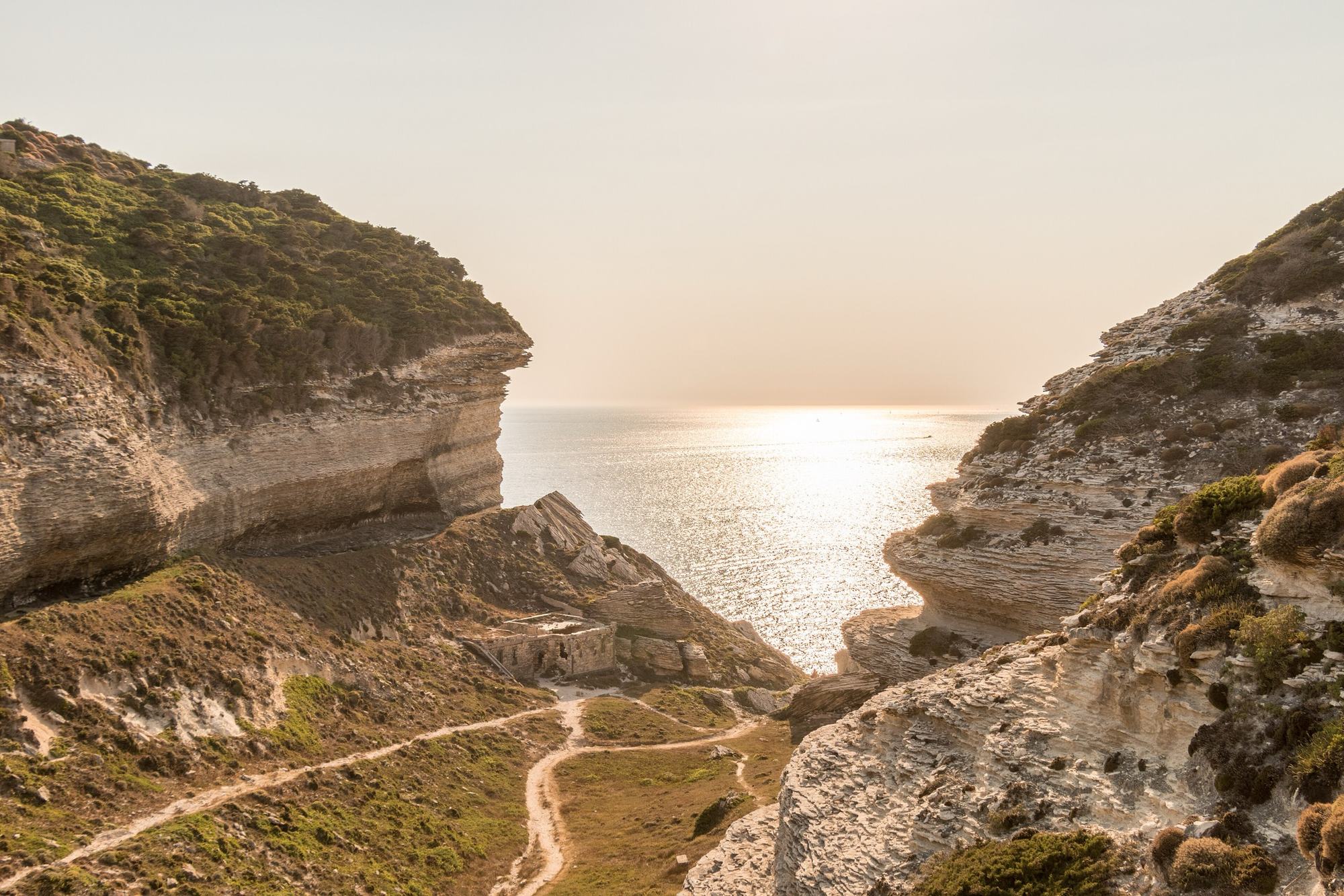 Une piste de terre serpente entre deux falaises corses face à la mer au couchant